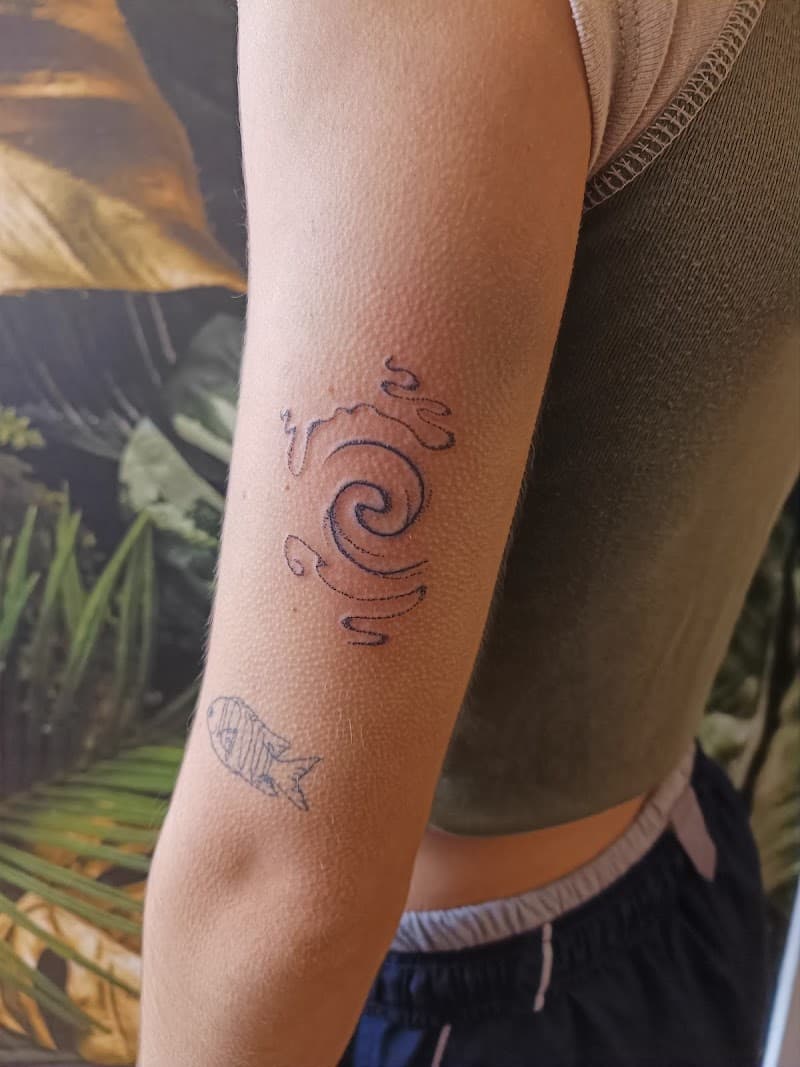 Abstracte spiraal en kleine vis fineline tattoos op bovenarm.