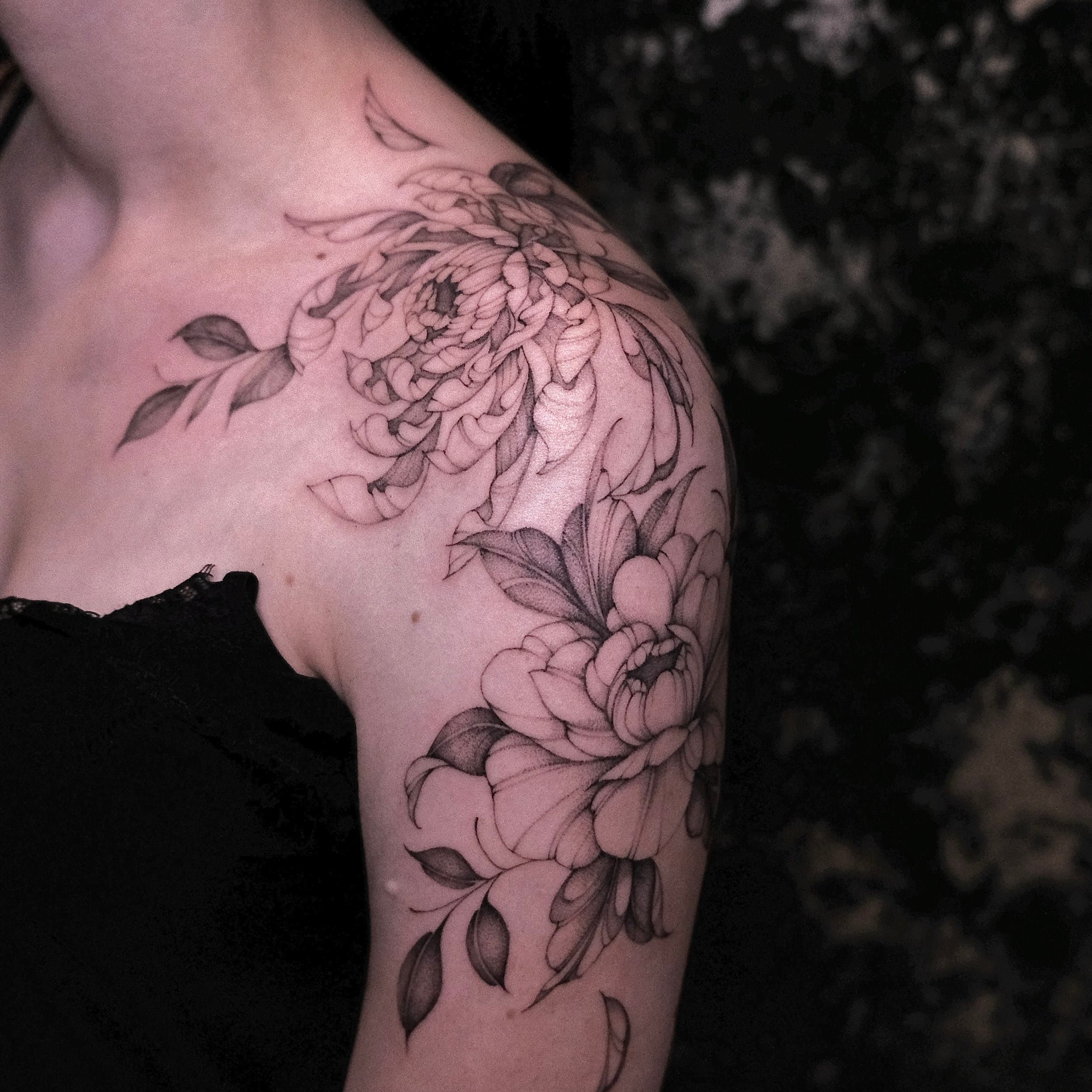 Fineline bloemen tattoo op schouder en bovenarm.