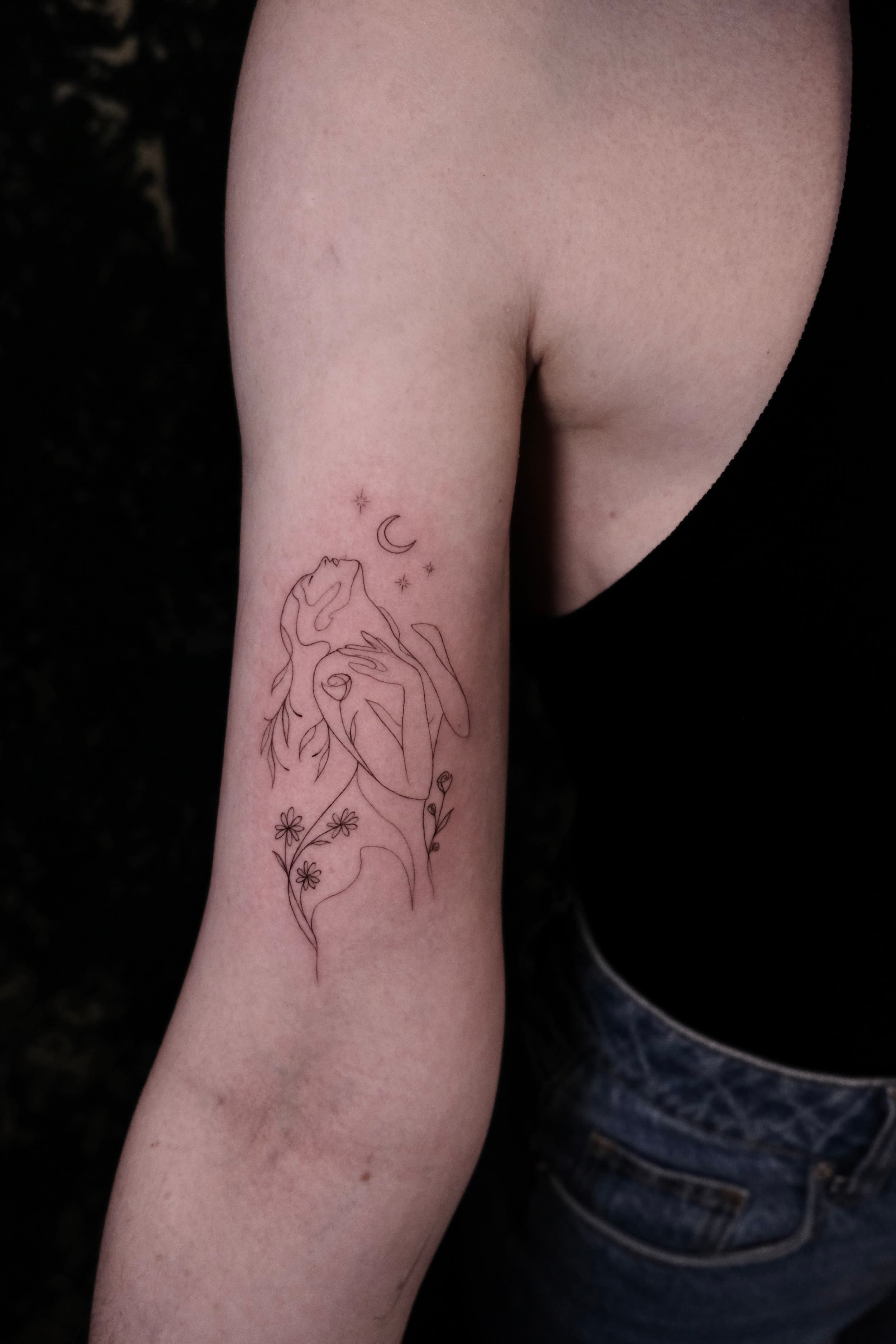 Fineline tattoo van een vrouwensilhouet met bloemen, maan en sterren.