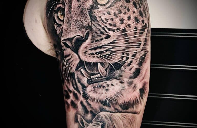 Realistische zwart-wit tattoo van een luipaardkop op de bovenarm.