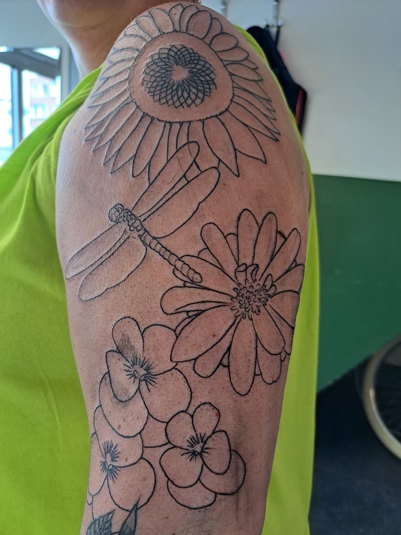 Fineline tattoo van zonnebloem, libel, madeliefje en viooltjes op bovenarm.
