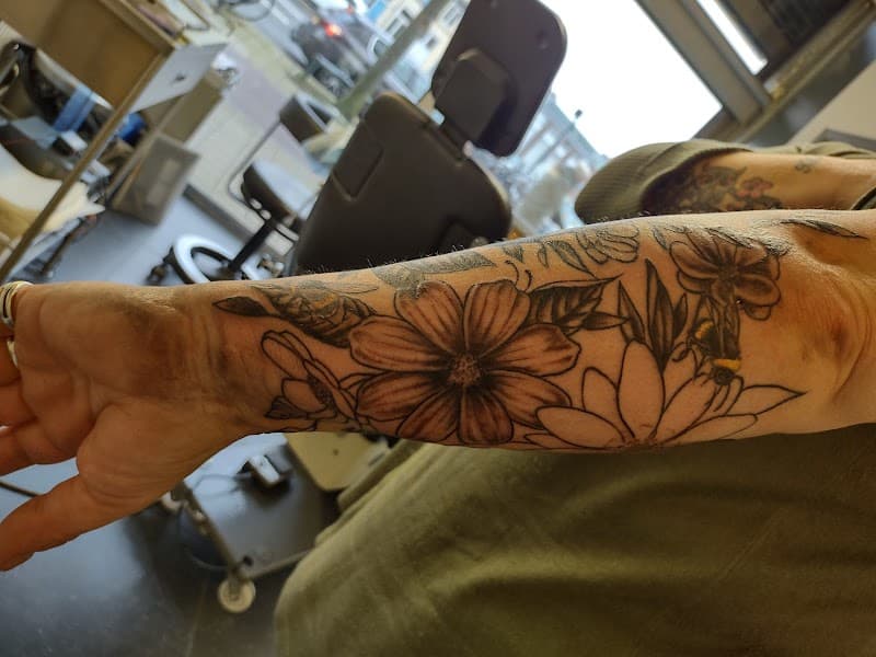 Illustratieve bloemen en bij tattoo op onderarm.