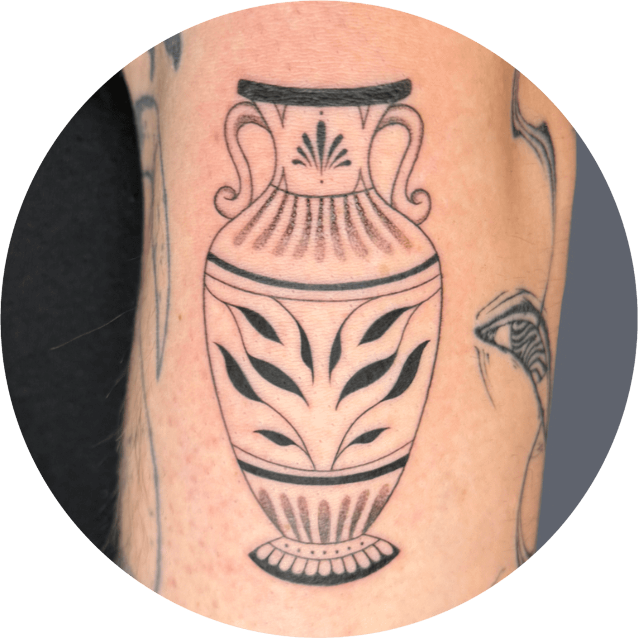 Zwart-wit illustratieve tattoo van een Griekse vaas met bladmotief.
