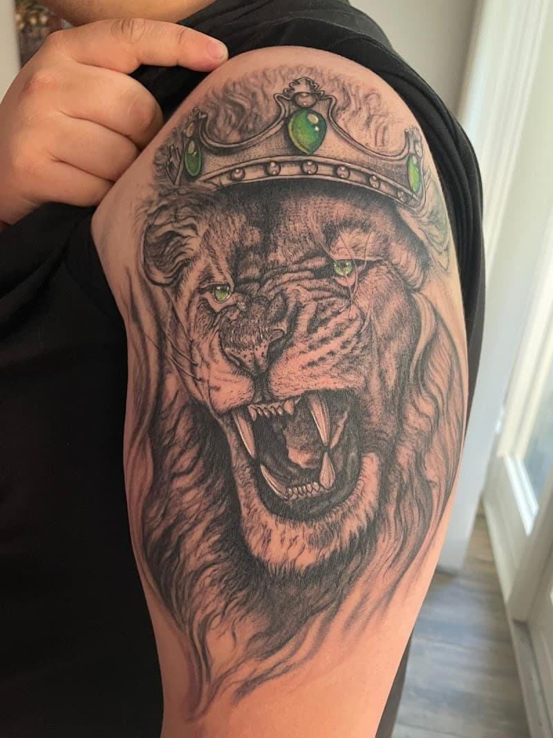 Realistische leeuw met kroon en groene ogen op bovenarm.