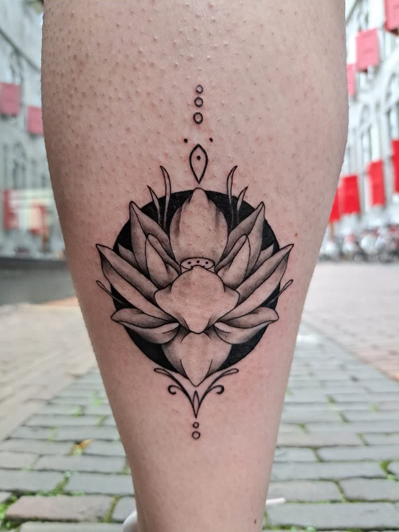 Blackwork lotusbloem in cirkel met ornamenten op kuit.