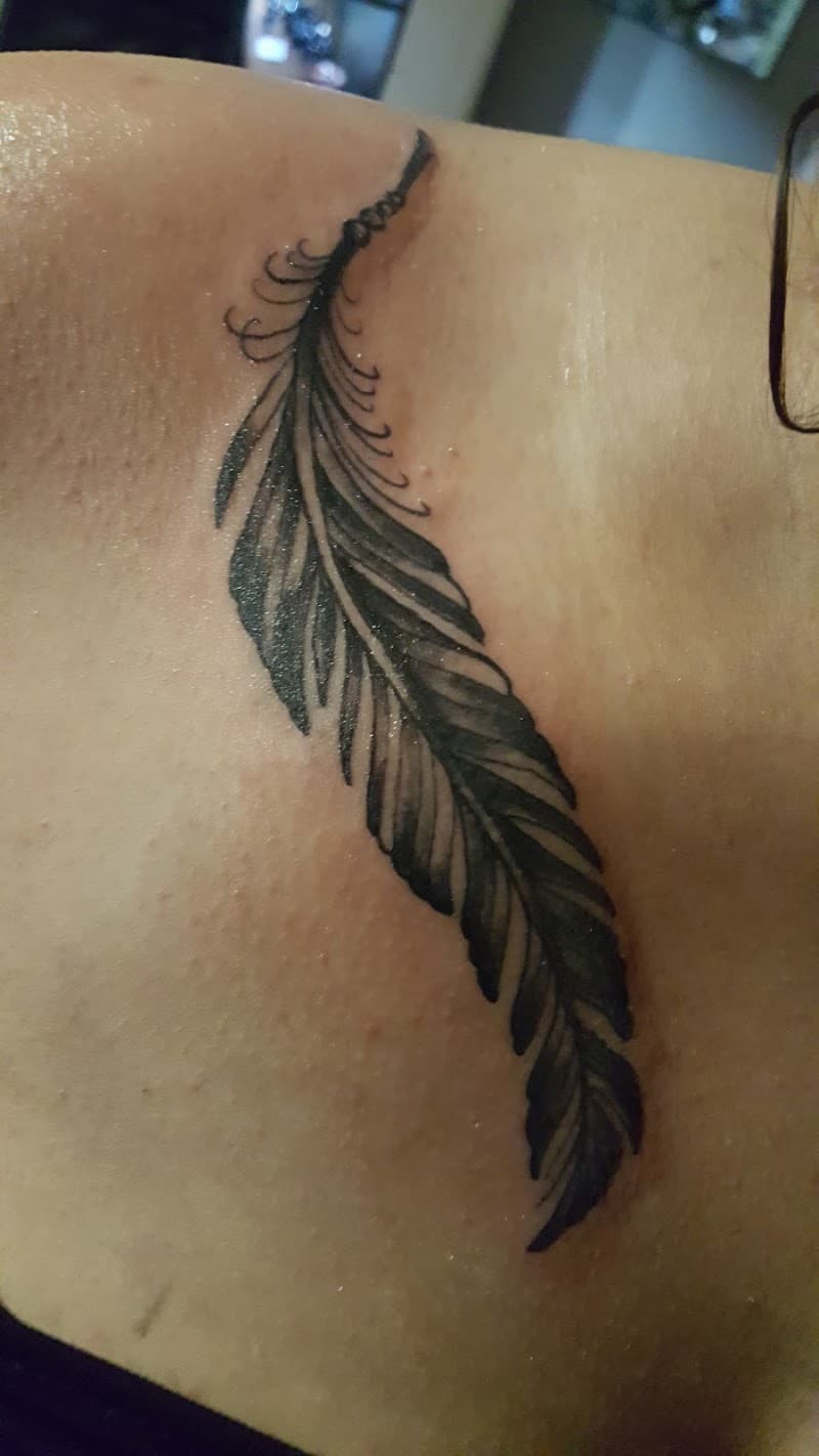 Gedetailleerde zwart-witte veer tattoo op de schouder.