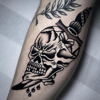 Traditionele tattoo van een schedel doorboord met een dolk en een takje.