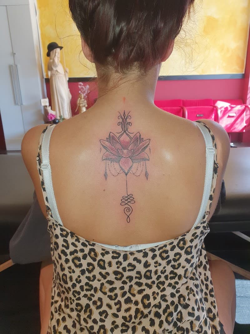 Fineline lotus met unalome en dotwork op de bovenrug.