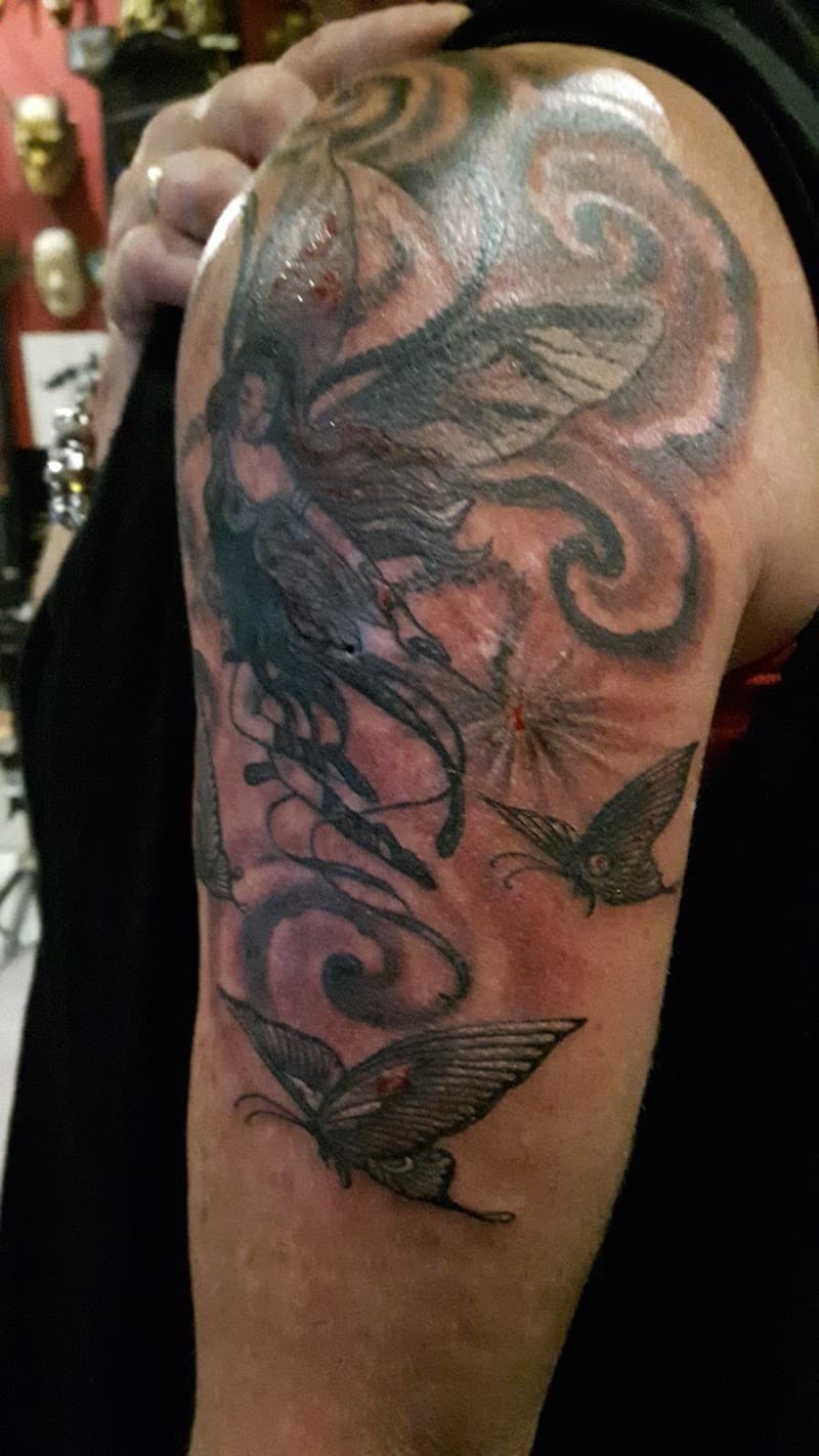 Zwart-grijze fee en vlinders met krullen op bovenarm.