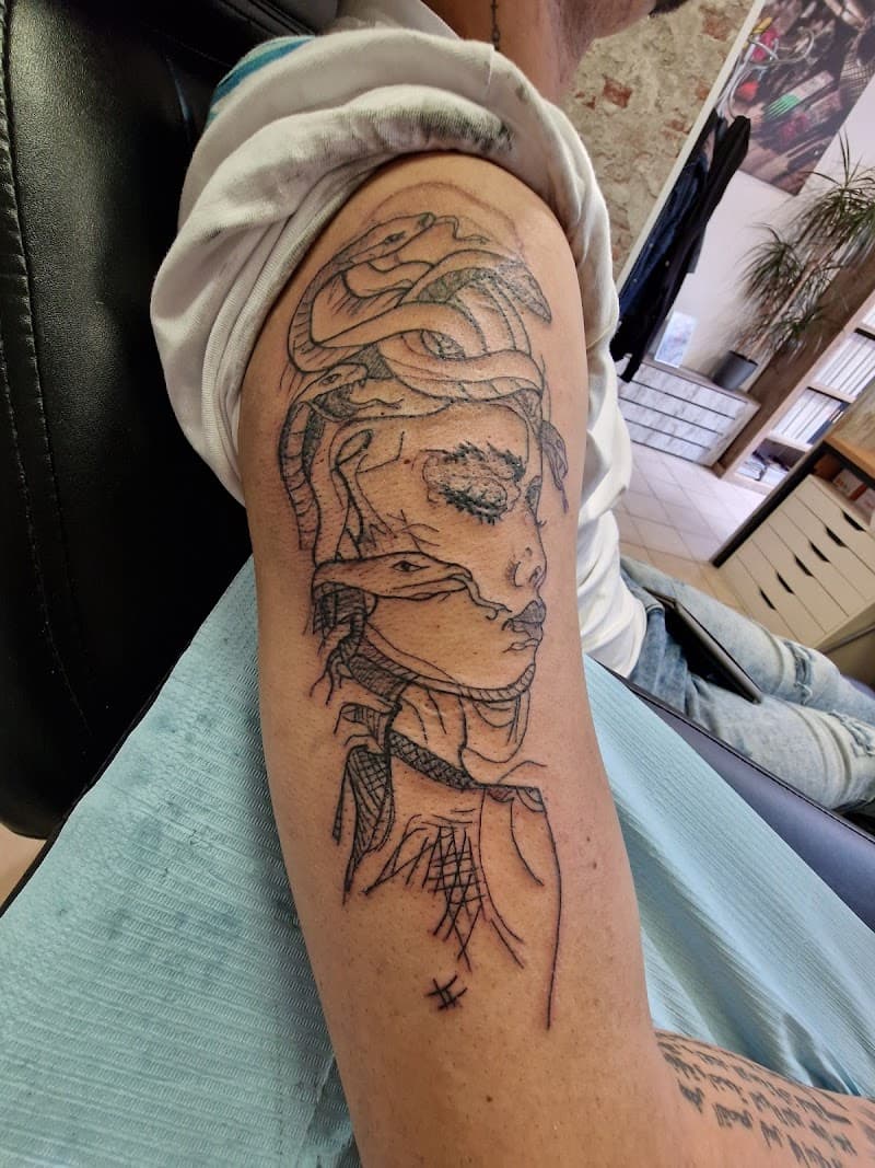 Fineline schets tattoo van Medusa met slangenhaar op bovenarm.