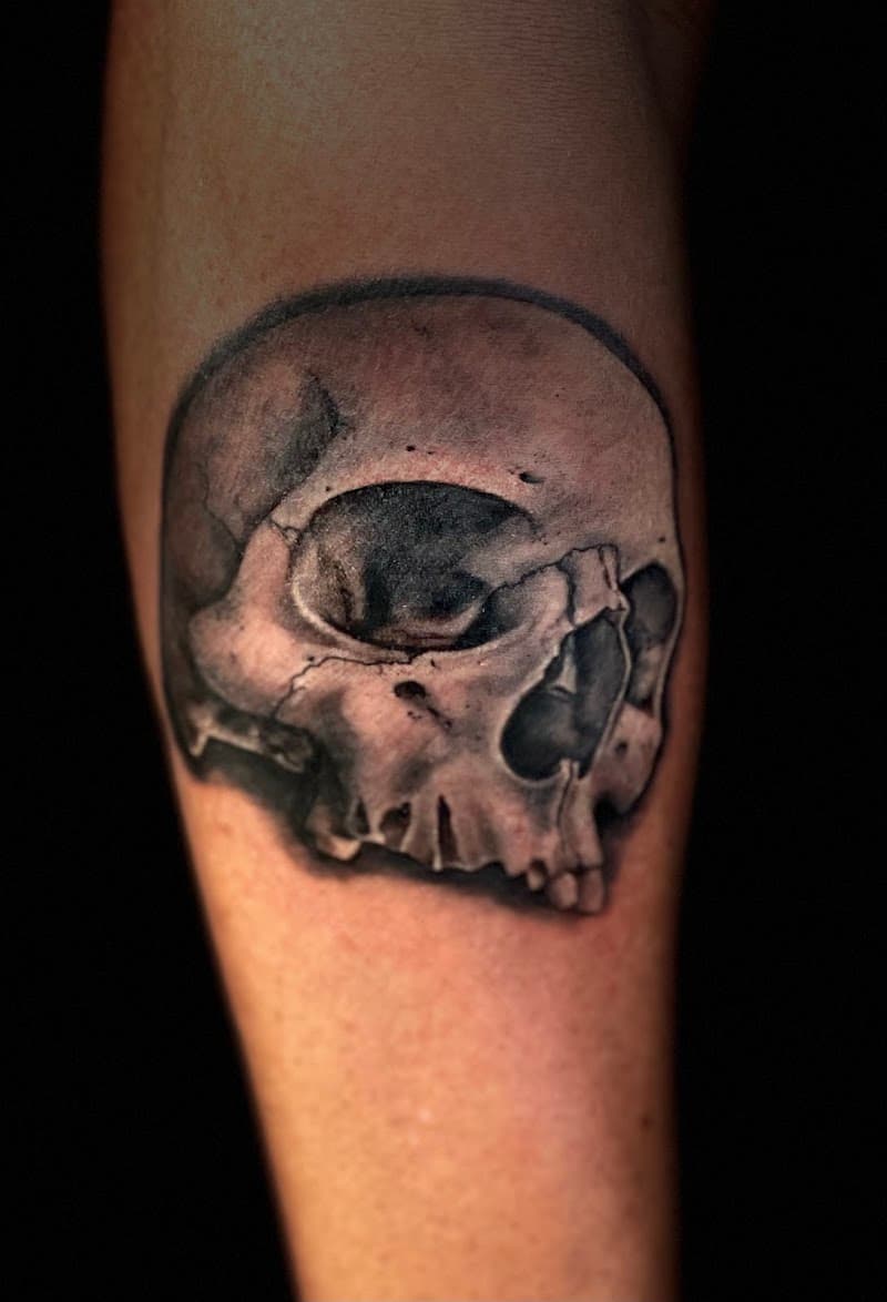 Realistische schedel tattoo in zwart-wit op de onderarm.