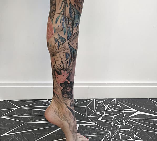 Kleurrijke onderwater tattoo met axolotl en vissen op onderbeen.