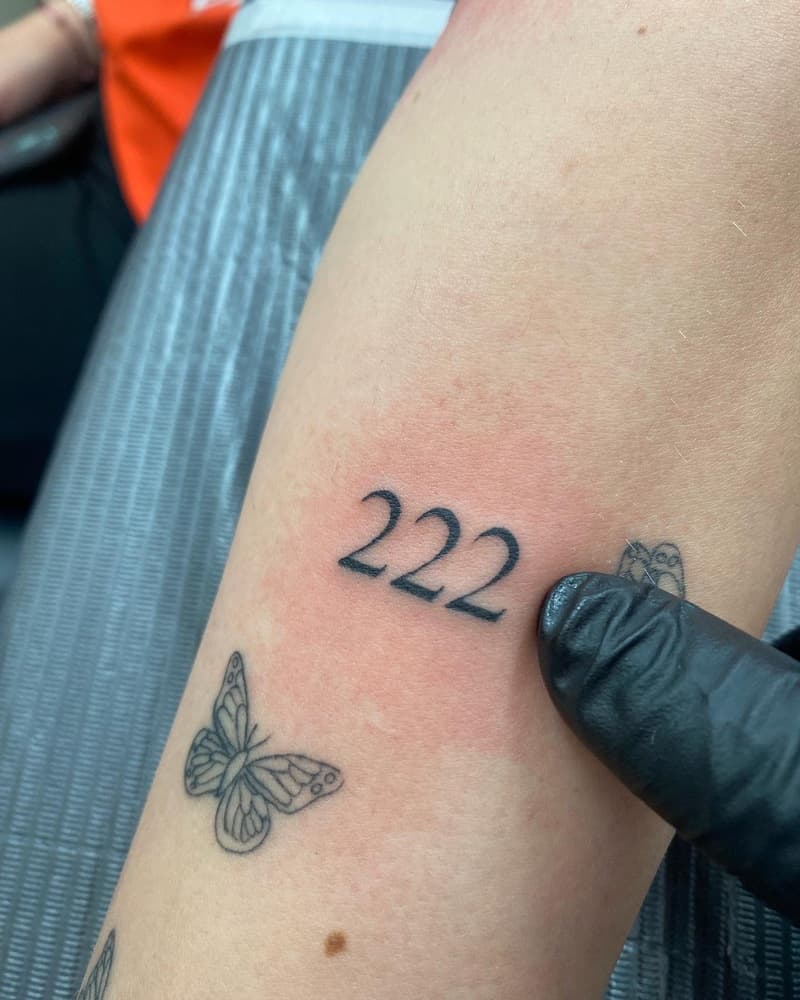 Fineline '222' nummer tattoo en twee vlinders op onderarm.