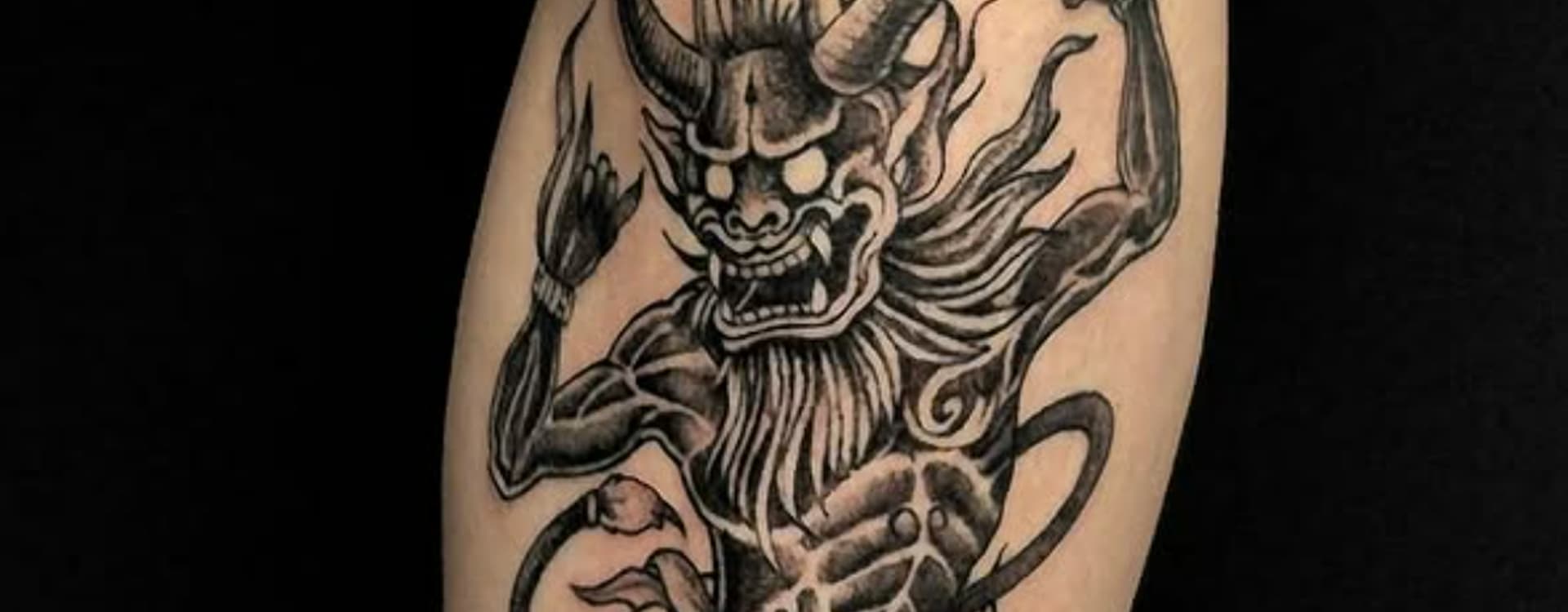 Zwart-wit blackwork tattoo van een Japanse Oni demon op het onderbeen.