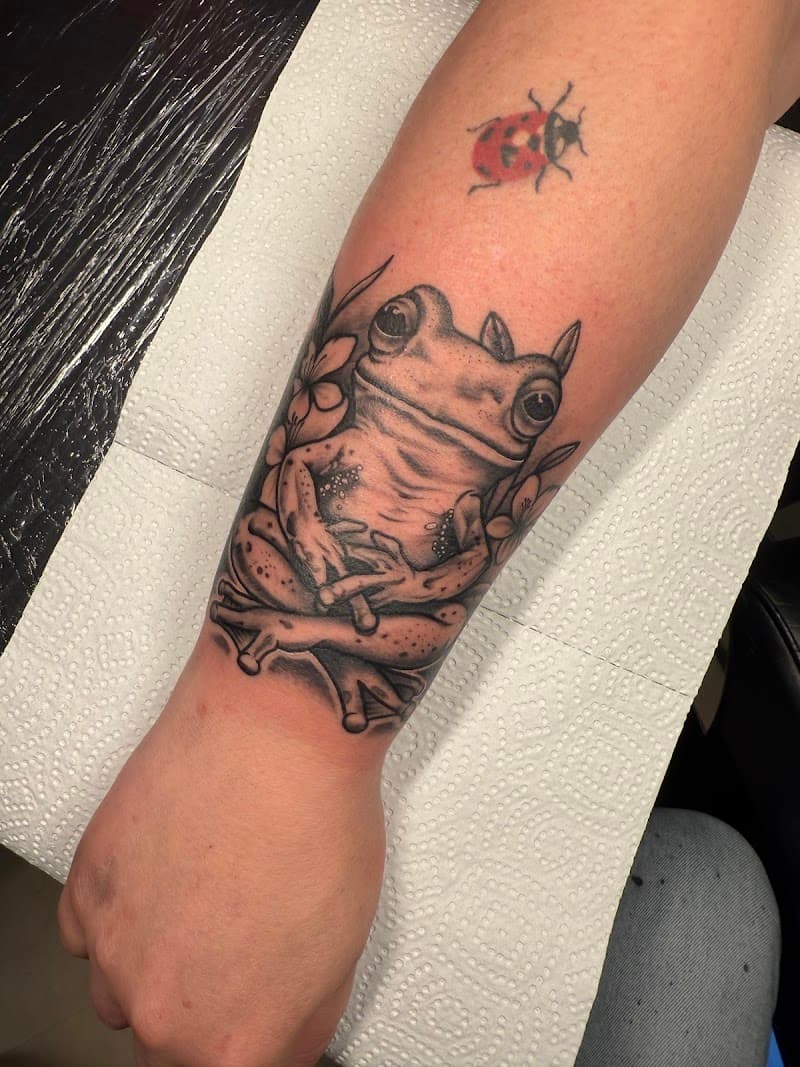 Zwart-wit kikker in lotushouding en een kleine gekleurde lieveheersbeestje tattoo.