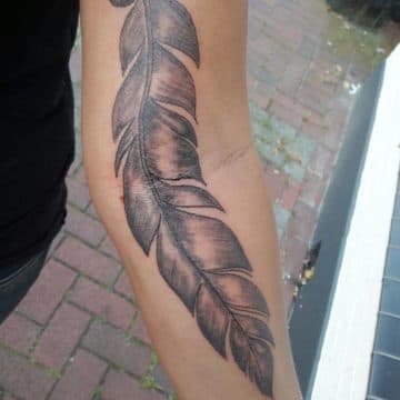 Grote, gedetailleerde veer tattoo in black & grey op de onderarm.