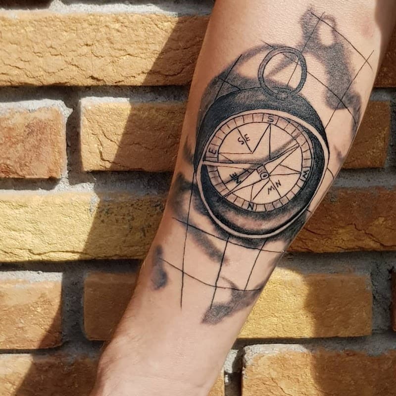 Zwart-wit kompas tattoo met wereldkaart op onderarm.