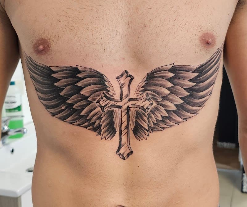 Zwart-wit tattoo van een kruis met grote vleugels op de borst en buik.