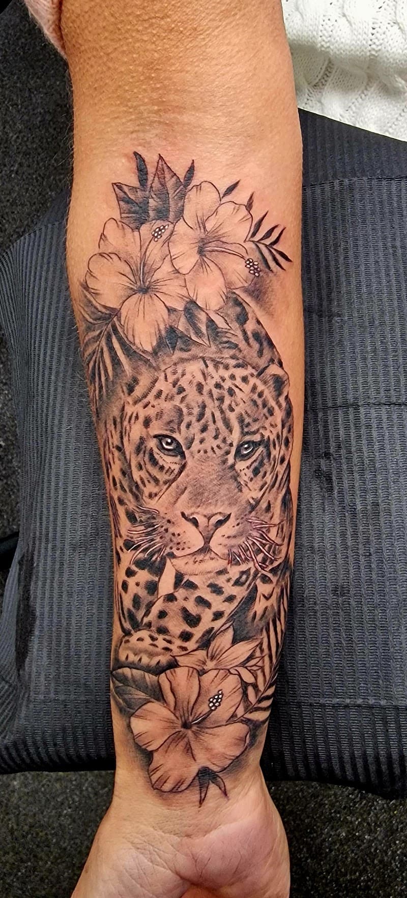 Realistische luipaard met hibiscus bloemen op onderarm.
