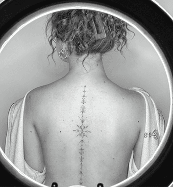 Fijne lijn ornamentale tattoo langs de ruggengraat.
