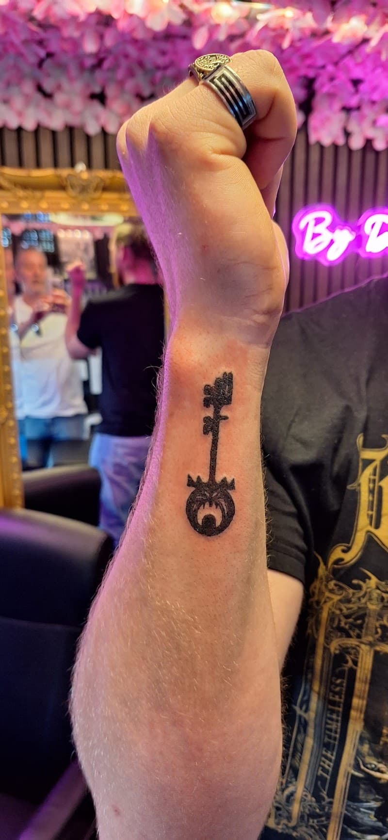 Zwarte sleutel tattoo met een kroon en een oog in de baard, op de pols.