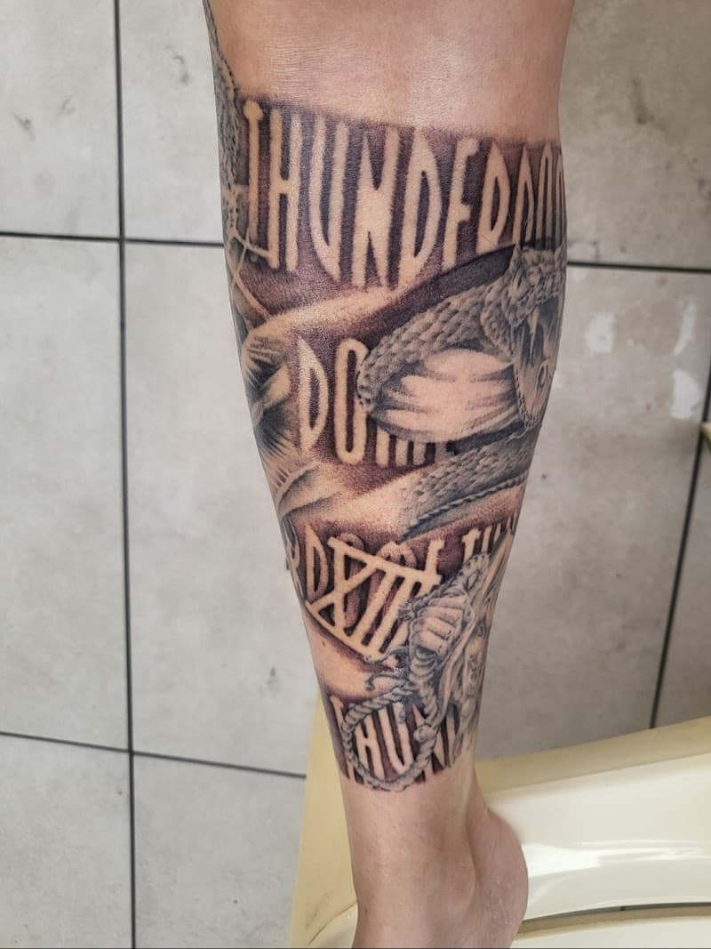 Zwart-wit tattoo op onderbeen met tekst "THUNDERDOME" en een slang.