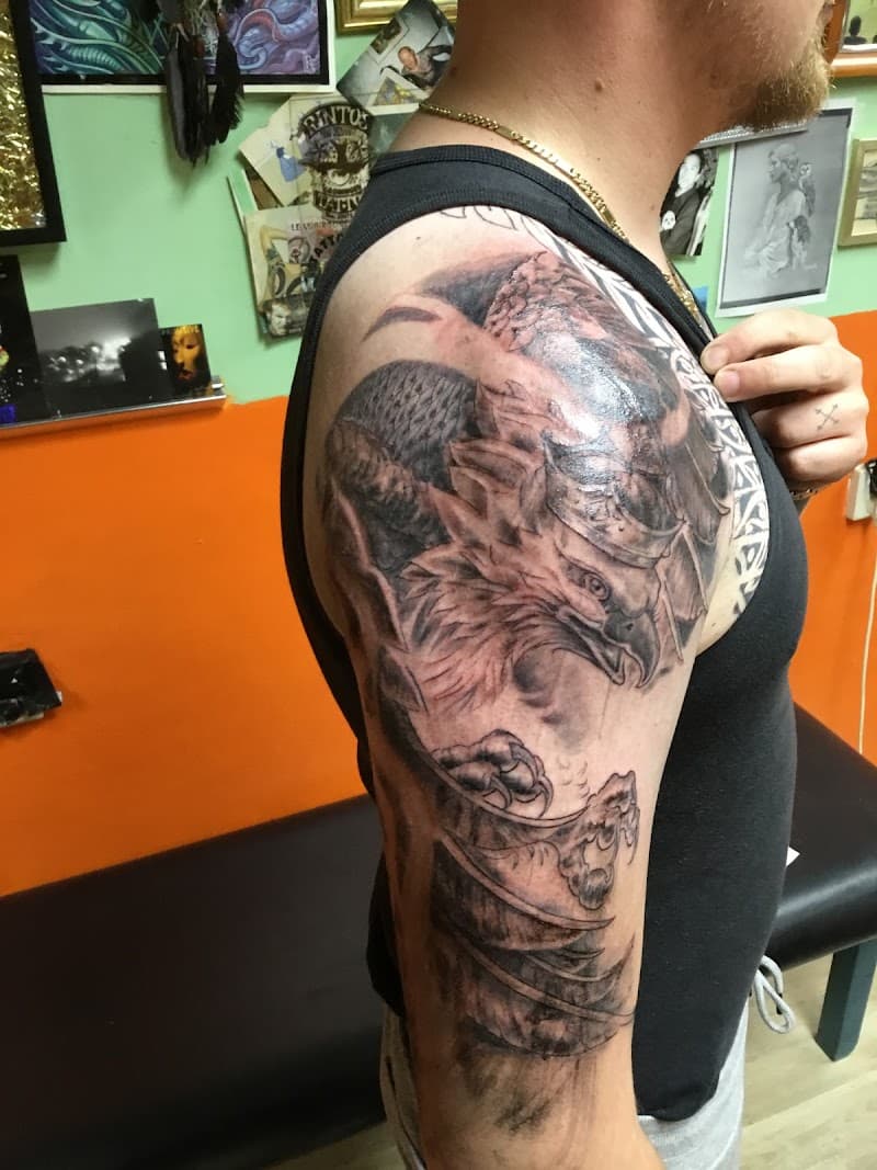 Grote zwart-wit griffioen tattoo op bovenarm en schouder.