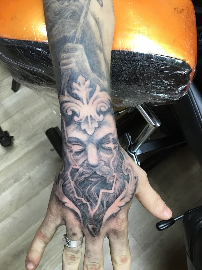 Zwart-wit tattoo van een bebaard gezicht (Zeus/Poseidon) op de hand.