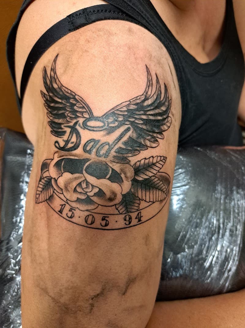 Zwart-wit tattoo met 'Dad', vleugels, roos en datum 15.05.94.