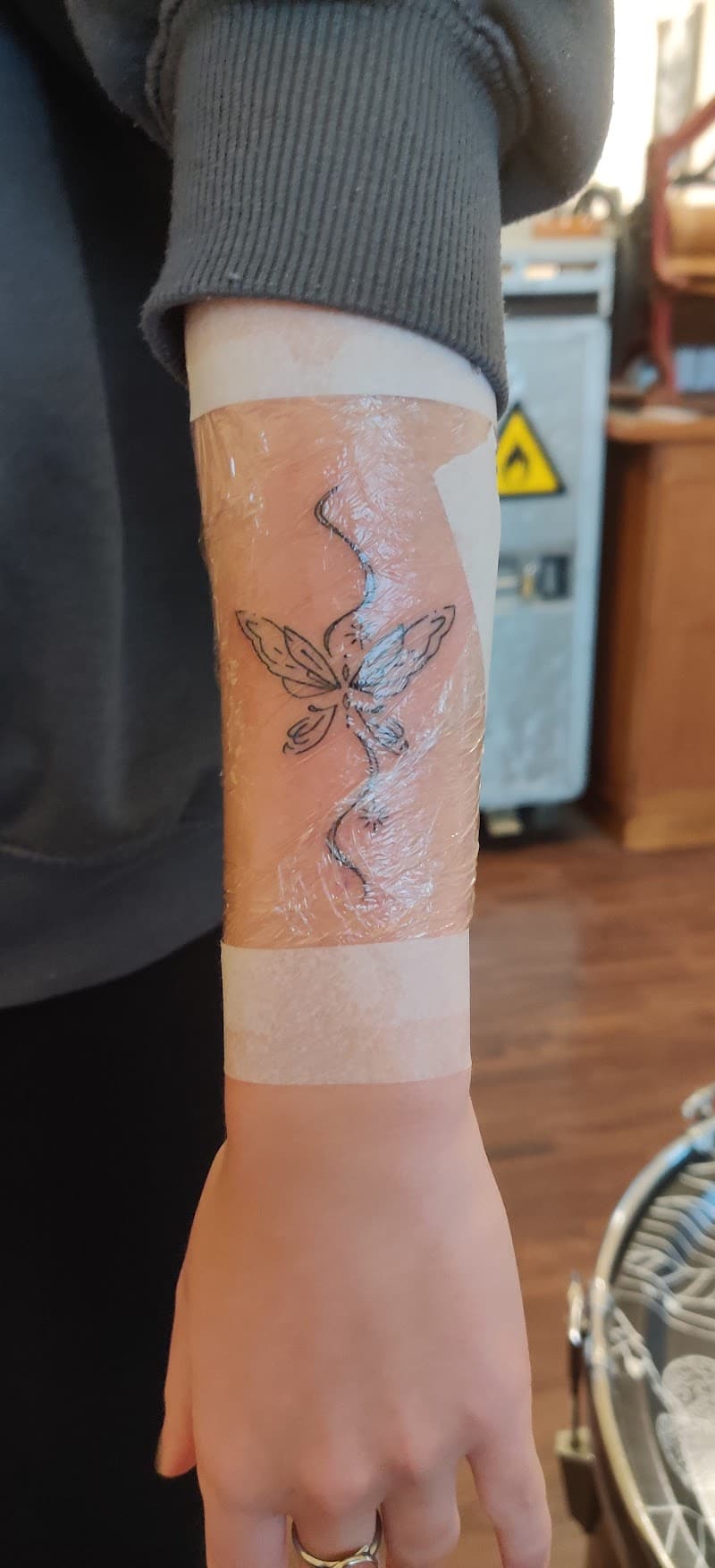Fineline vlinder met sierlijke lijn op onderarm, vers gezet.