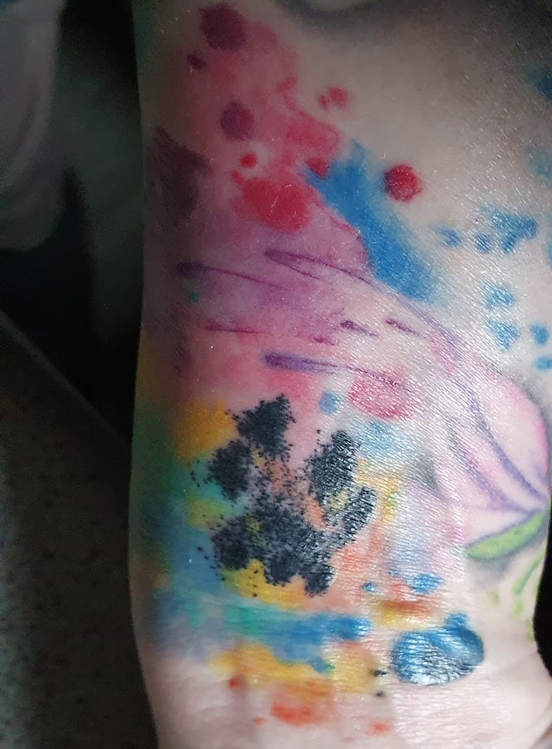 Kleurrijke watercolor hondenpoot tattoo op de enkel.
