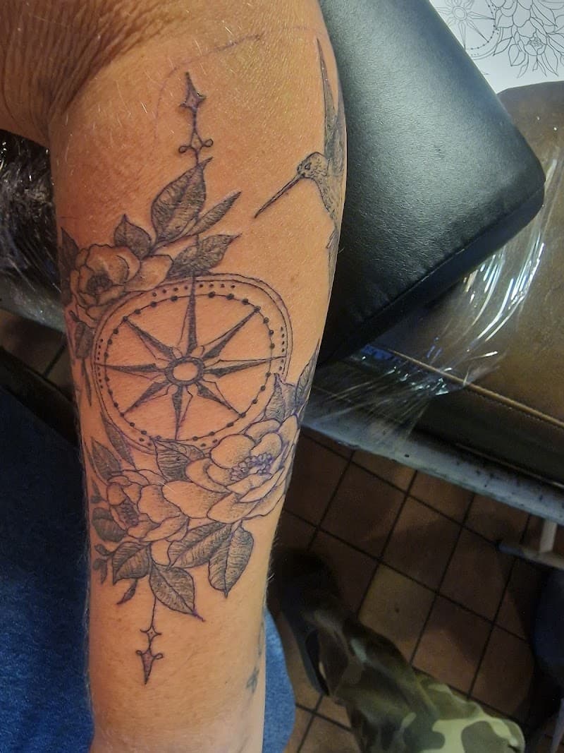 Kompas met bloemen en kolibrie in fineline op onderarm.