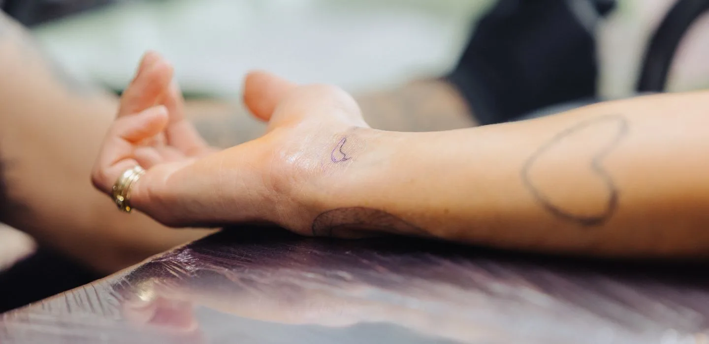 Kleine 'C' of halve maan tattoo op de pols, met een hart en een andere tattoo op de onderarm.