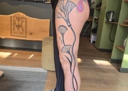 Grote fineline bloemen en een gekleurde veer op het bovenbeen.