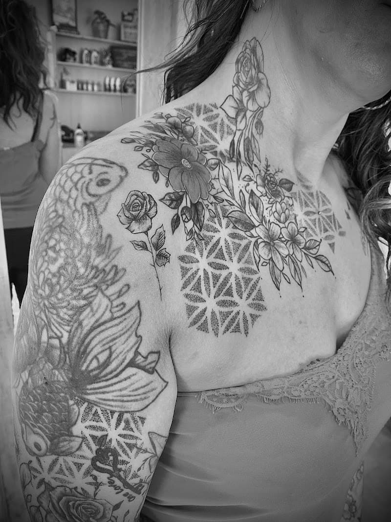 Zwart-wit tattoo op schouder, nek en borst met bloemen en geometrisch dotwork.