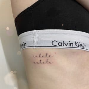 Fineline 'inhale exhale' tekst op de ribben.