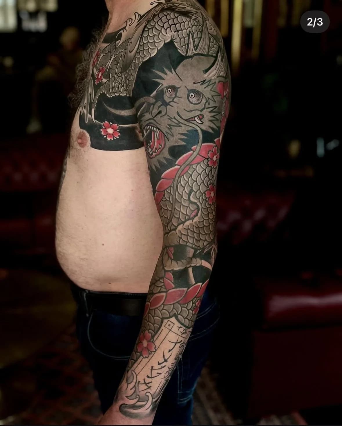 Japanse draak sleeve tattoo met kersenbloesems en tekst.