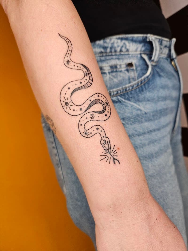 Fineline slang met sterren en maan op onderarm.