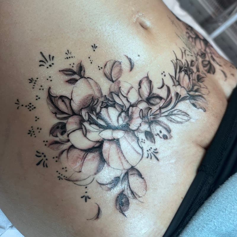 Zwart-wit bloementattoo met dotwork details op de buik en heup.