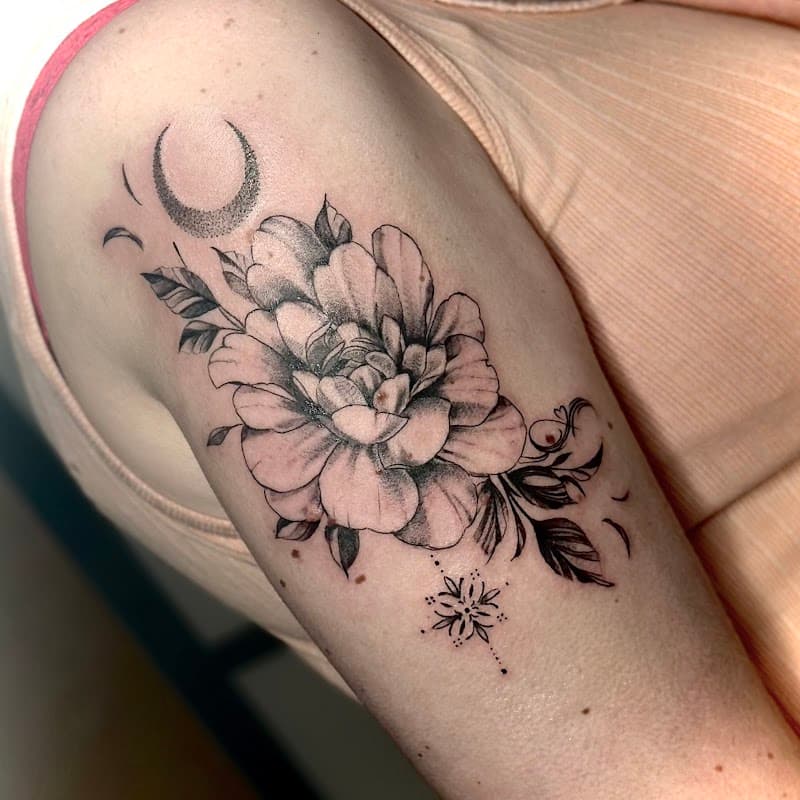 Zwart-wit tatoeage van een pioenroos met een halve maan en ster op de bovenarm.
