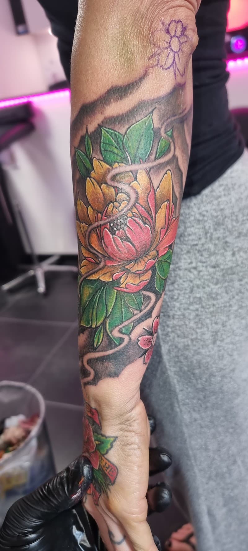 Kleurrijke neo-traditional bloem met bladeren en slang op onderarm.