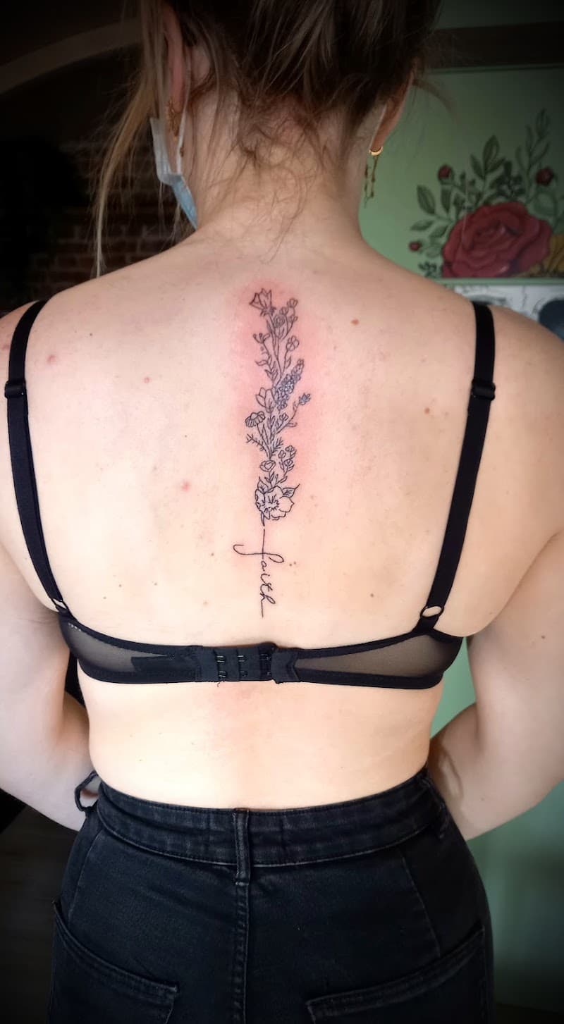 Fineline bloemenstengel met 'faith' tekst op de ruggengraat.