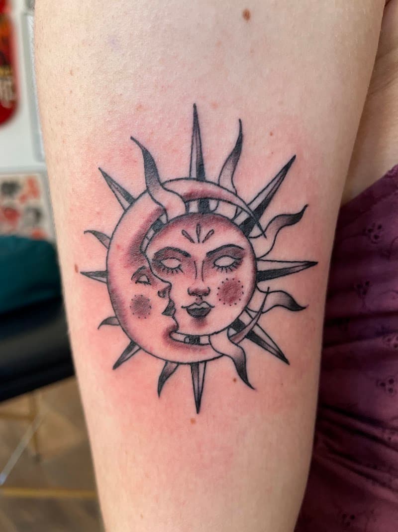 Zon en maan met gezichten, in elkaar verstrengeld op de bovenarm.