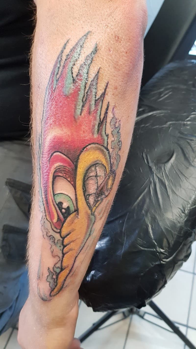 Kleurrijke cartoon tattoo van een vogelkop met vlammen op de onderarm.