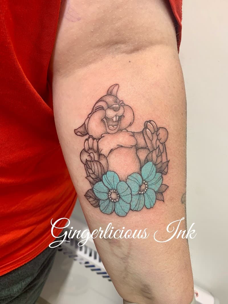 Vrolijke Thumper tattoo met twee turquoise bloemen op de bovenarm.