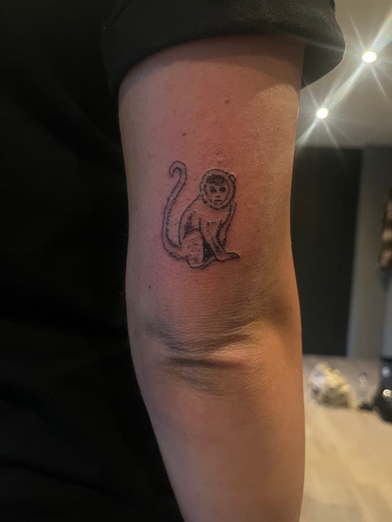 Kleine, minimalistische aap tattoo op de bovenarm.