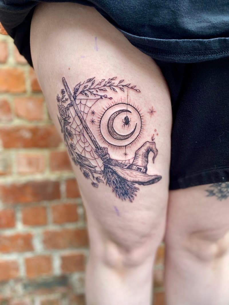 Fineline tattoo van heksenhoed, bezem, maan en spin op bovenbeen.
