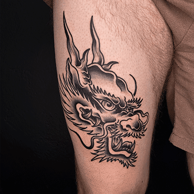 Close-up van een Japanse drakenkop tattoo in zwart-wit op het bovenbeen.