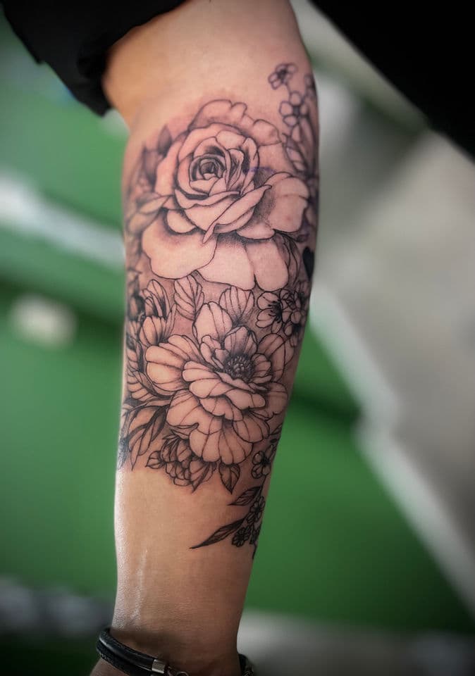 Blackwork bloemen tattoo met roos en pioenroos op onderarm.