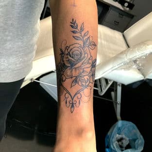 Zwart-wit roos met bladeren en sierlijke lijnen op onderarm.